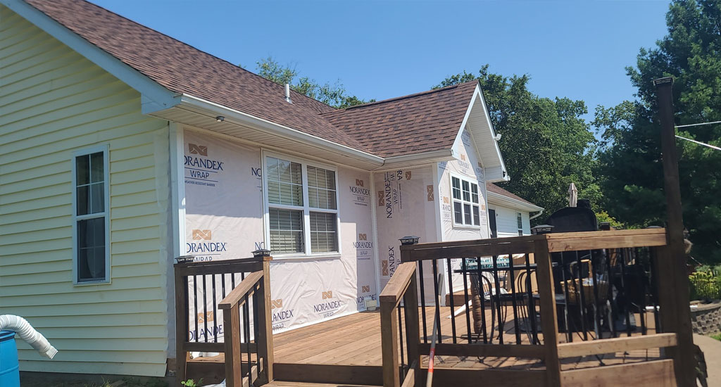 Siding installation in progress on a home, with new siding and house wrap visible